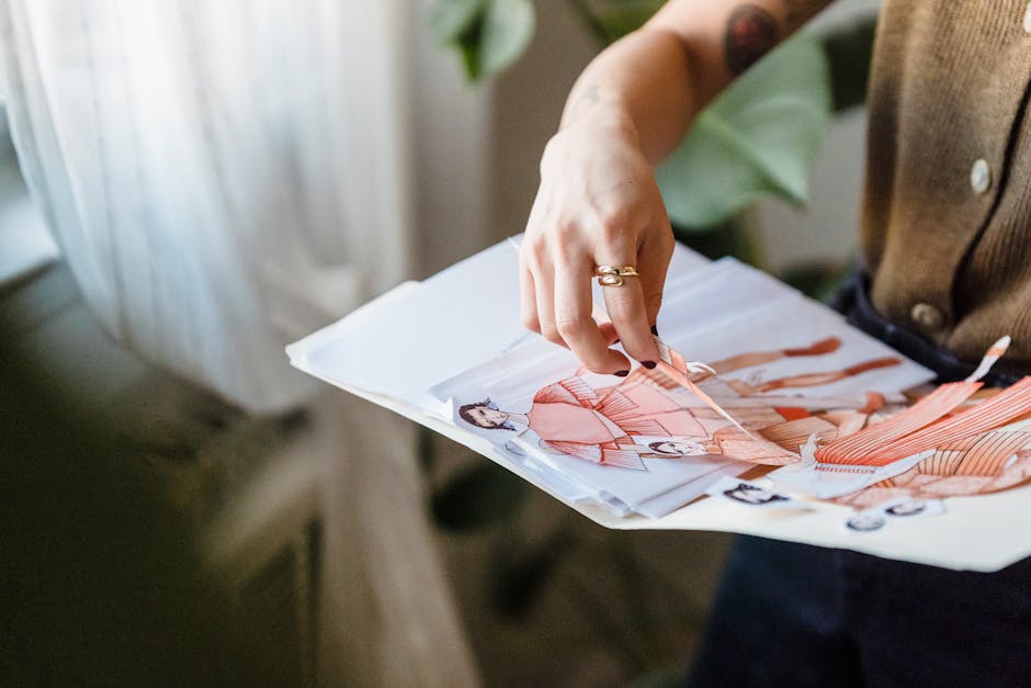From above of crop anonymous female dressmaker choosing cut out fashion sketches from folder during work in modern studio